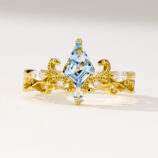 Regal two-tone sterling silver ring featuring a large kite-cut light blue topaz stone at the center, surrounded by round brilliant-cut white cubic zirconia stones, set in an intricate gold-plated band with ornate scrollwork details, creating a majestic and eye-catching look perfect for adding a touch of royalty to any outfit.