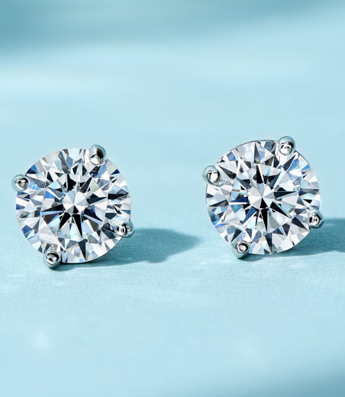 Timeless Four-Prong Sterling Silver Stud Earrings with Round Clear Gemstones A pair of round-cut clear gemstone stud earrings in a four-prong sterling silver setting, displayed against a soft blue background