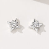 A pair of star-shaped stud earrings in polished sterling silver, featuring a central clear gemstone surrounded by six pointed silver rays, creating a celestial and sparkling design.