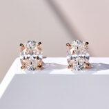 A pair of oval-cut clear gemstone stud earrings in a four-prong rose gold-toned setting, displayed against a soft white background.