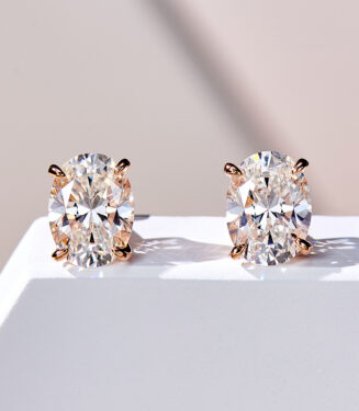 A pair of oval-cut clear gemstone stud earrings in a four-prong rose gold-toned setting, displayed against a soft white background.