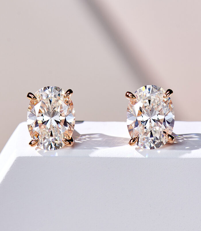 Elegant Oval-Cut Rose Gold-plated Stud Earrings with Clear Gemstones A pair of oval-cut clear gemstone stud earrings in a four-prong rose gold-toned setting, displayed against a soft white background.