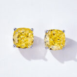A pair of cushion-cut yellow diamond stud earrings in a four-prong sterling silver setting, displayed against a soft white background.