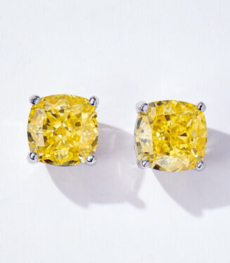 A pair of cushion-cut yellow diamond stud earrings in a four-prong sterling silver setting, displayed against a soft white background.