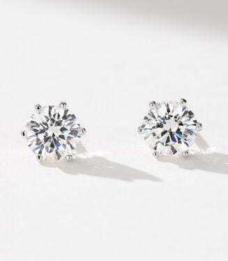 A pair of round, brilliant-cut stud earrings in polished sterling silver, featuring a central clear gemstone set in a classic six-prong setting, displayed against a soft white background.