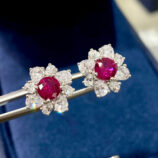 Sterling silver stud earrings with a round-cut red gemstone center surrounded by a halo of clear stones.