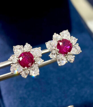 Sterling silver stud earrings with a round-cut red gemstone center surrounded by a halo of clear stones.