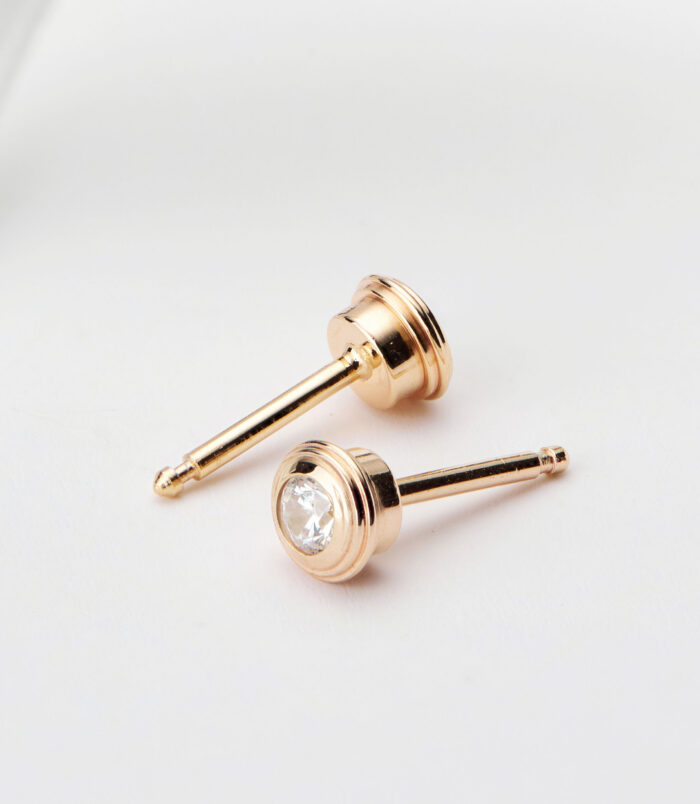 Sterling silver stud earrings with a round clear cubic zirconia center stone and a polished gold-toned setting