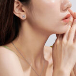 A pair of square, princess-cut stud earrings in polished sterling silver, featuring a central clear gemstone set in a sleek four-prong setting, displayed on a model's ear against a soft, neutral background.