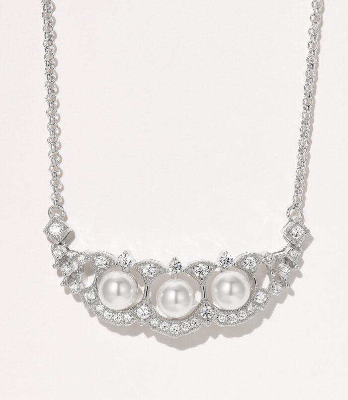 Elegant sterling silver necklace featuring a curved bar pendant adorned with three round white freshwater pearls, surrounded by a halo of round brilliant-cut white cubic zirconia stones, creating a sophisticated and timeless look perfect for adding a touch of classic elegance to any outfit.