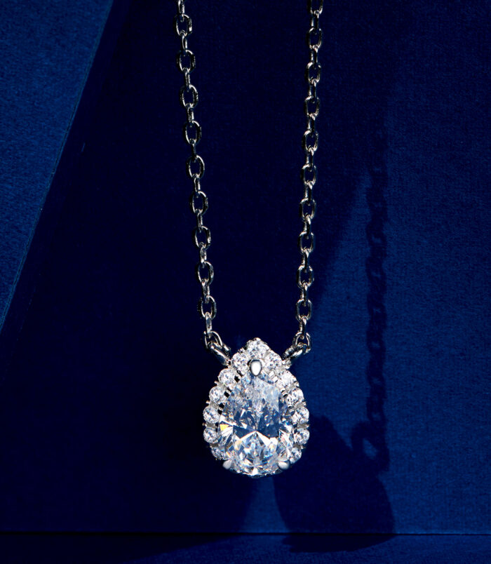 Stunning sterling silver solitaire necklace, featuring a large pear-shaped brilliant-cut white cubic zirconia stone in a halo setting surrounded by smaller round brilliant-cut white cubic zirconia stones, paired with a classic cable chain, creating a glamorous and sophisticated look perfect for adding a touch of luxury to any outfit.