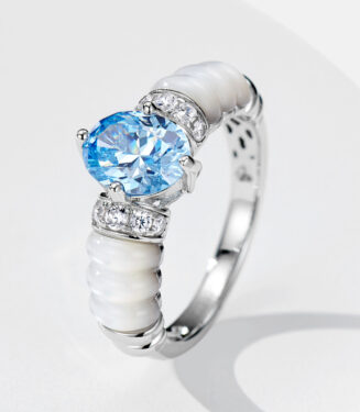 Unique sterling silver cocktail ring featuring a large oval-cut sky blue cubic zirconia center stone set in a four-prong setting, flanked by two rows of round brilliant-cut white cubic zirconia stones, with a distinctive white enamel segmented band, creating a bold and eye-catching look perfect for making a statement and adding a touch of glamour to any outfit.