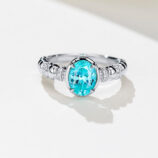Vintage-inspired sterling silver ring with a vibrant oval-cut paraiba tourmaline center stone, set in a bezel setting, and accented with milgrain details and pavé-set cubic zirconia along the twisted rope band for a unique and elegant look.