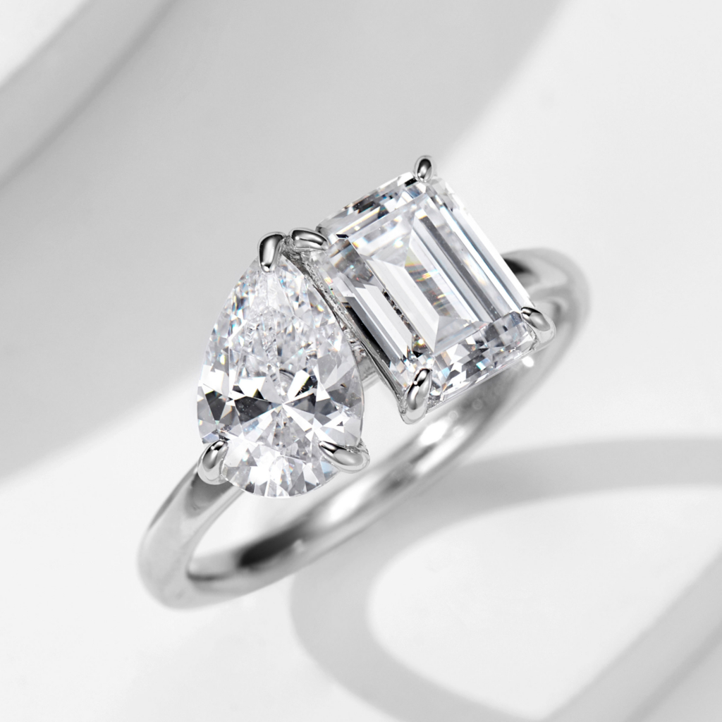 Elegant two-stone sterling silver ring featuring a large pear-shaped brilliant-cut white cubic zirconia stone and an emerald-cut white cubic zirconia stone set in a sleek and modern band, creating a sophisticated and eye-catching look perfect for engagements, anniversaries, or special occasions.