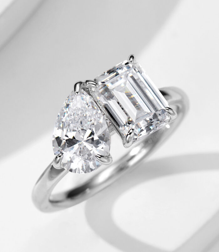 Elegant two-stone sterling silver ring featuring a large pear-shaped brilliant-cut white cubic zirconia stone and an emerald-cut white cubic zirconia stone set in a sleek and modern band, creating a sophisticated and eye-catching look perfect for engagements, anniversaries, or special occasions.