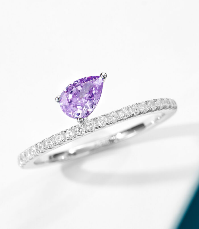 Elegant sterling silver engagement ring featuring a single pear-cut amethyst cubic zirconia center stone set in a four-prong setting, paired with a pavé-set band of round brilliant-cut white cubic zirconia stones, creating a romantic and feminine look perfect for engagements, anniversaries, or adding a touch of color to everyday wear.