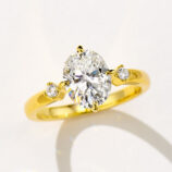 Stunning gold-plated sterling silver ring featuring a large oval-cut cubic zirconia center stone in a four-prong setting, flanked by two round brilliant-cut cubic zirconia accents on a polished band for a luxurious and elegant look.