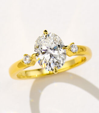 Stunning gold-plated sterling silver ring featuring a large oval-cut cubic zirconia center stone in a four-prong setting, flanked by two round brilliant-cut cubic zirconia accents on a polished band for a luxurious and elegant look.