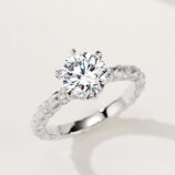 Rustic-inspired sterling silver engagement ring with a large round brilliant-cut cubic zirconia center stone in a four-prong setting, featuring a bark-textured band with pavé-set cubic zirconia accents for a nature-inspired and unique look.