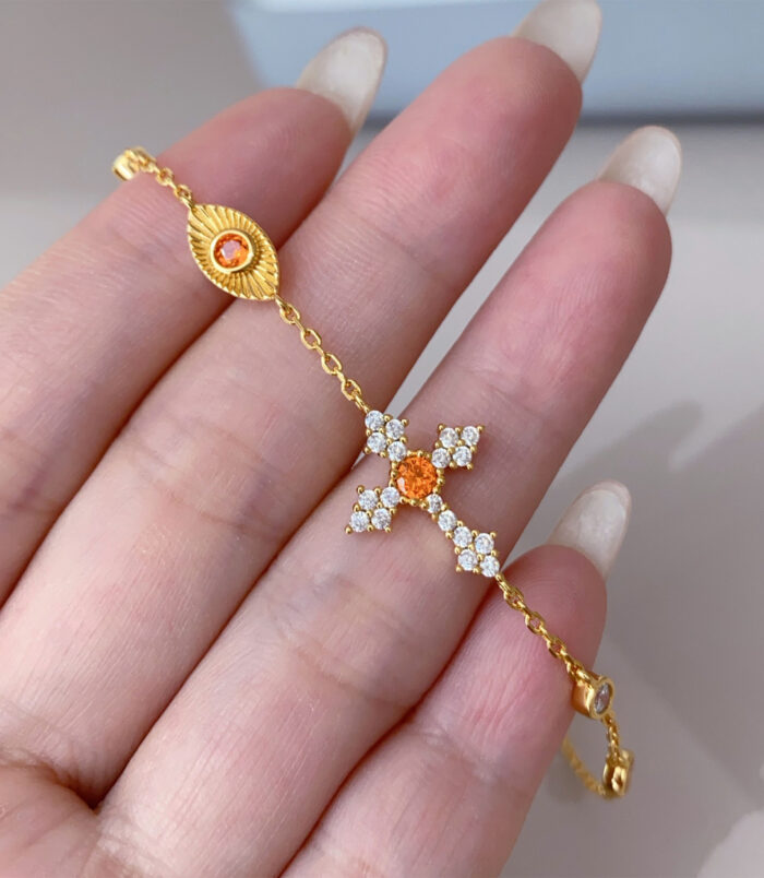 handheld close-up of orange cross silver bracelet, highlighting the details of cross cluster.