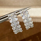 Use tweezers to hold the Sterling Silver Cubic Zirconia Huggie Hoop Earrings for display.
