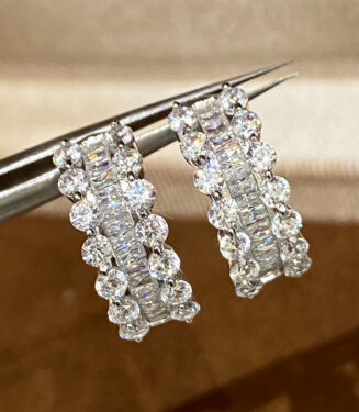 Use tweezers to hold the Sterling Silver Cubic Zirconia Huggie Hoop Earrings for display.