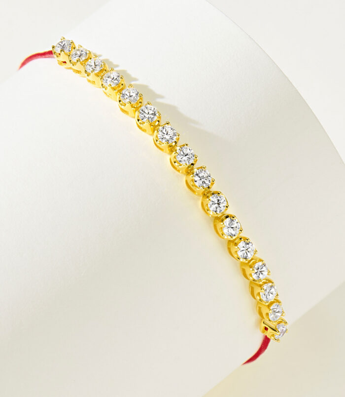 side view of gold plated 925 silver bracelet with cubic zirconia stones and a red string