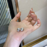 Pair of silver stud earrings with a central round stone and halo of small crystals, displayed on a woman’s hand