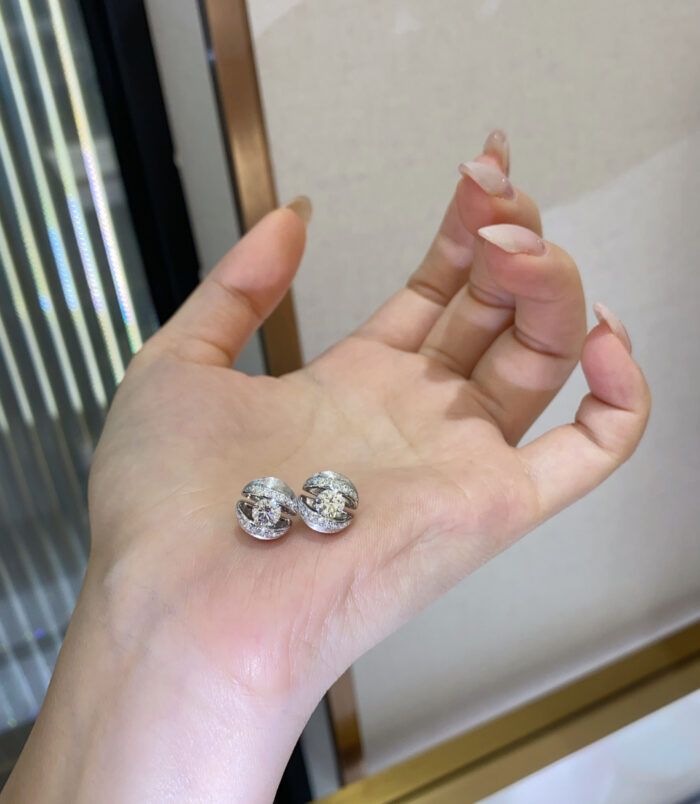 Pair of silver stud earrings with a central round stone and halo of small crystals, displayed on a woman’s hand