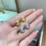 Set of gold and silver stud earrings with central round stones, displayed on a woman’s hand