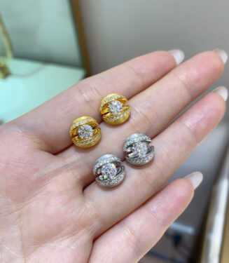 Set of gold and silver stud earrings with central round stones, displayed on a woman’s hand