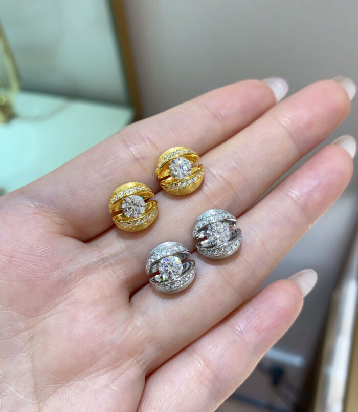 Set of gold and silver stud earrings with central round stones, displayed on a woman’s hand