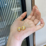 Pair of gold-plated silver stud earrings with a central round stone and halo of small crystals, displayed on a woman’s hand